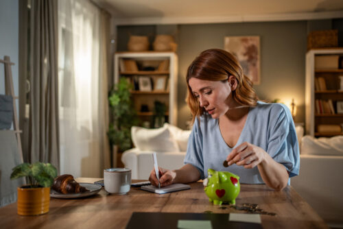 Woman sitting at a desk putting money in a piggy bank.