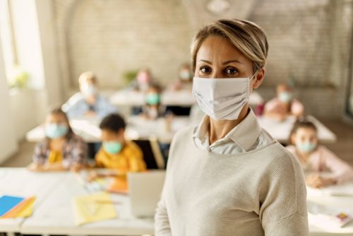 Elementary school teacher with protective face mask in the classroom.