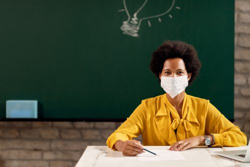 Black female teacher wearing face mask while giving a lecture in the classroom.