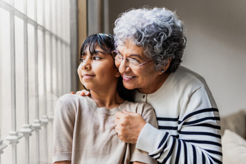 Grandmother and granddaughter looking through the window and contemplating at home