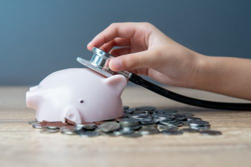 A hand holding a stethoscope listening to a broken piggy bank lying on a pile of coins. Financial health and financial status concept.