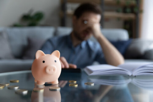 PIggybank on a table with man behind him expressing worry.