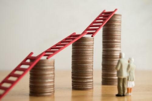 Older couple standing looking at stacks of money growing, representing growth and stability