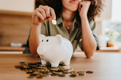 Young woman inserting her last coins in a piggy bank, worried about her financial situation