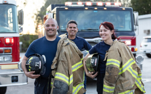 3 firefighters in front of a truck.